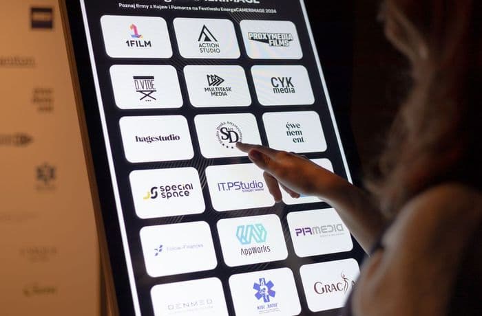 Osoba klika w logotyp znajdujący się na monitorze infokiosku. 