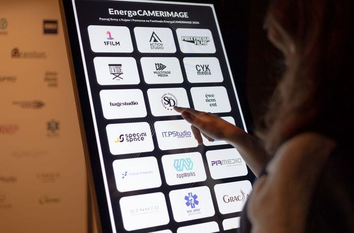 Osoba klika w logotyp znajdujący się na monitorze infokiosku. 